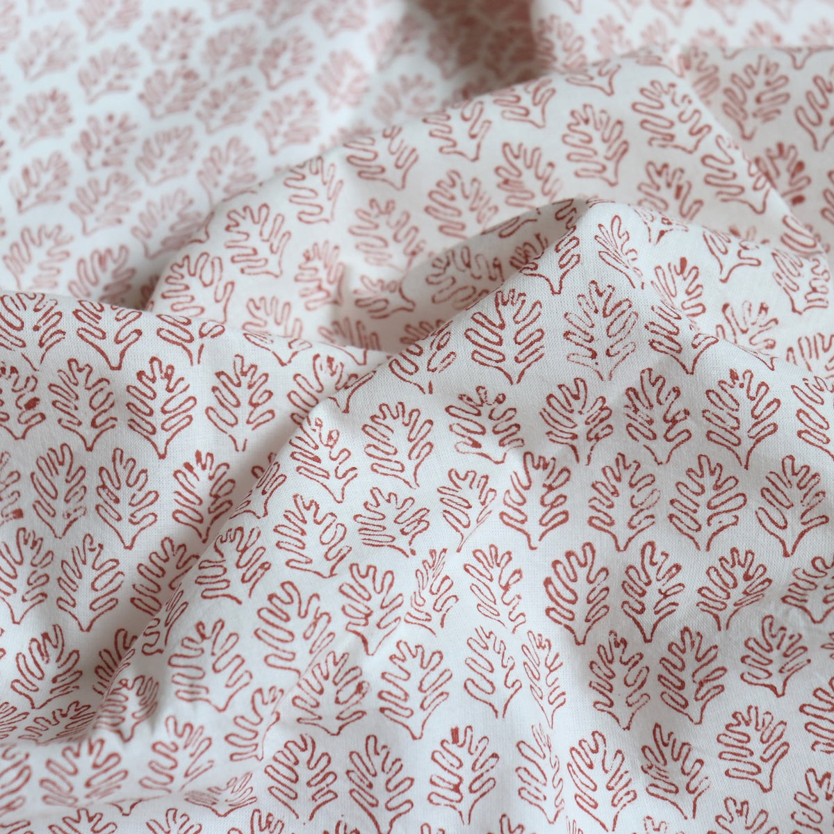soft white cotton fabric hand block printed with tiny red leaf shapes